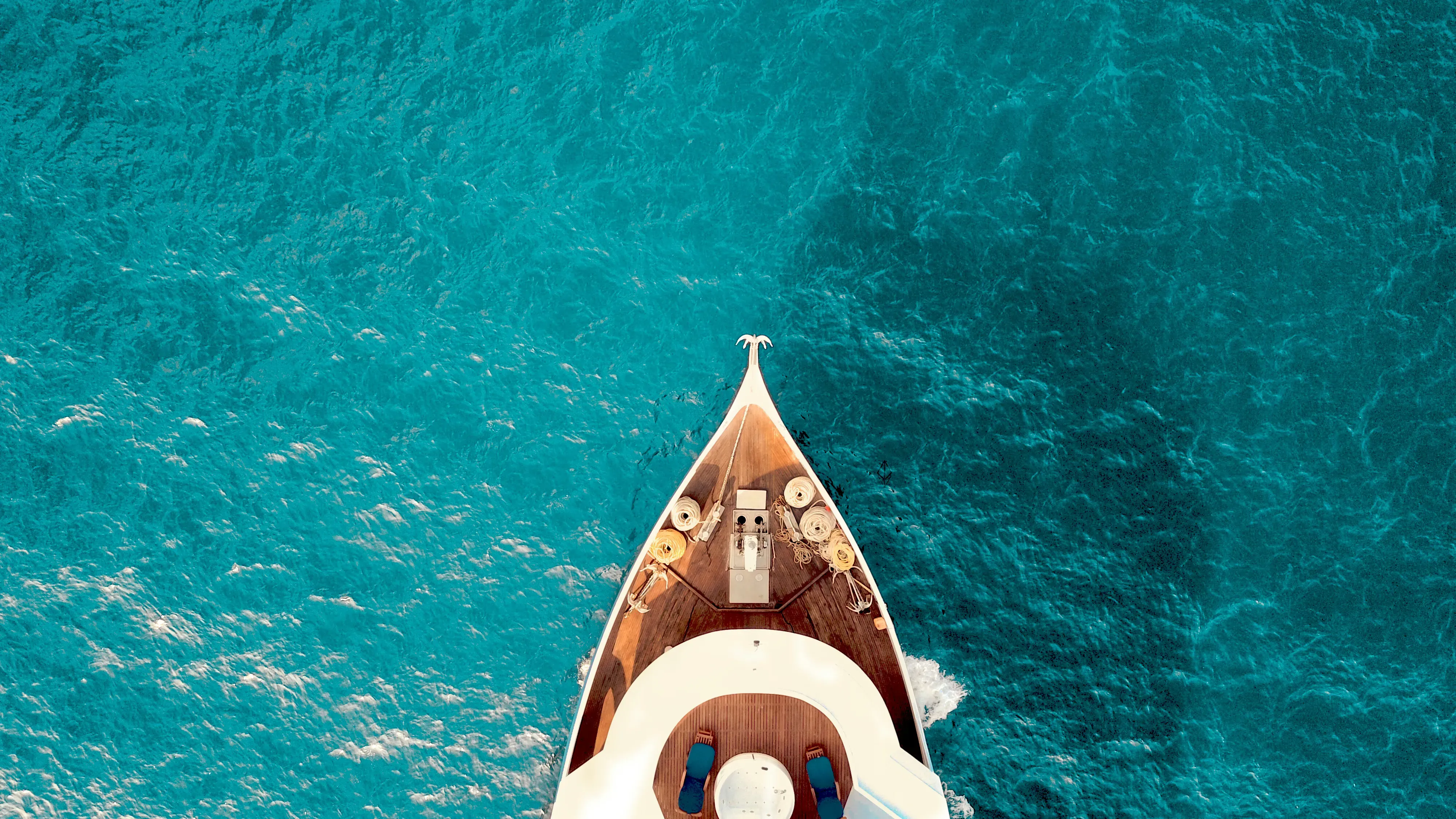 Aerial view of a luxury yacht bow cutting through crystal-clear turquoise water