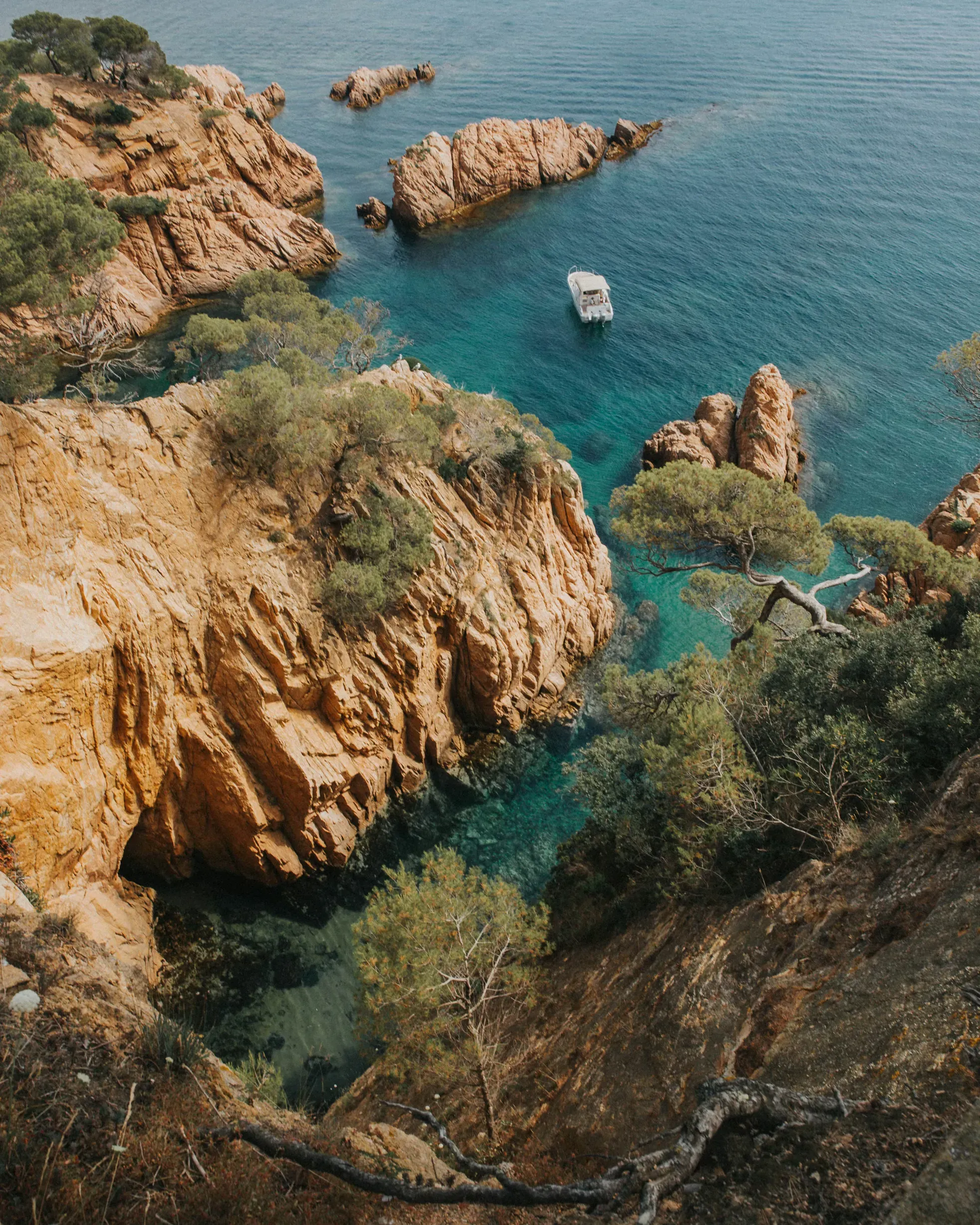Rocky Mediterranean coastline with turquoise water and a boat anchored in a secluded cove